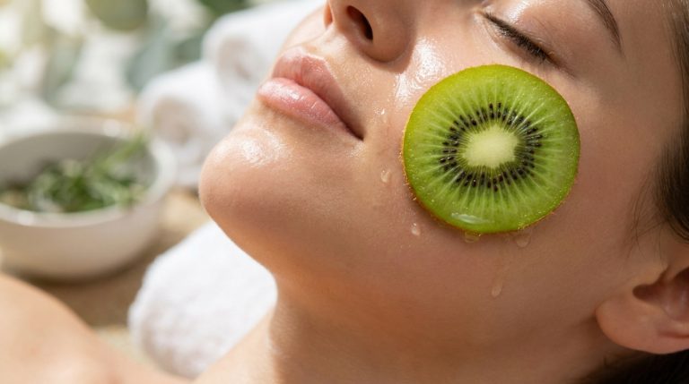 Gros plan sur le visage d'une femme détendue, une tranche de kiwi sur la joue. Peau hydratée avec des gouttes d'eau.